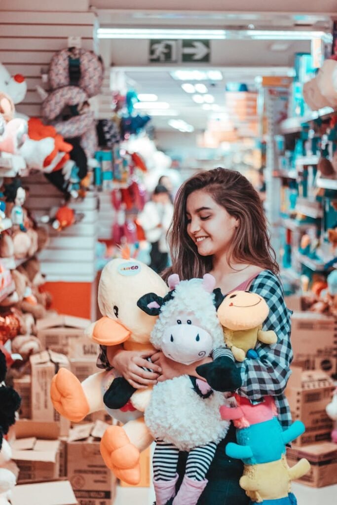 Woman smiling and holding various stuffed animals while shopping in a toy store.