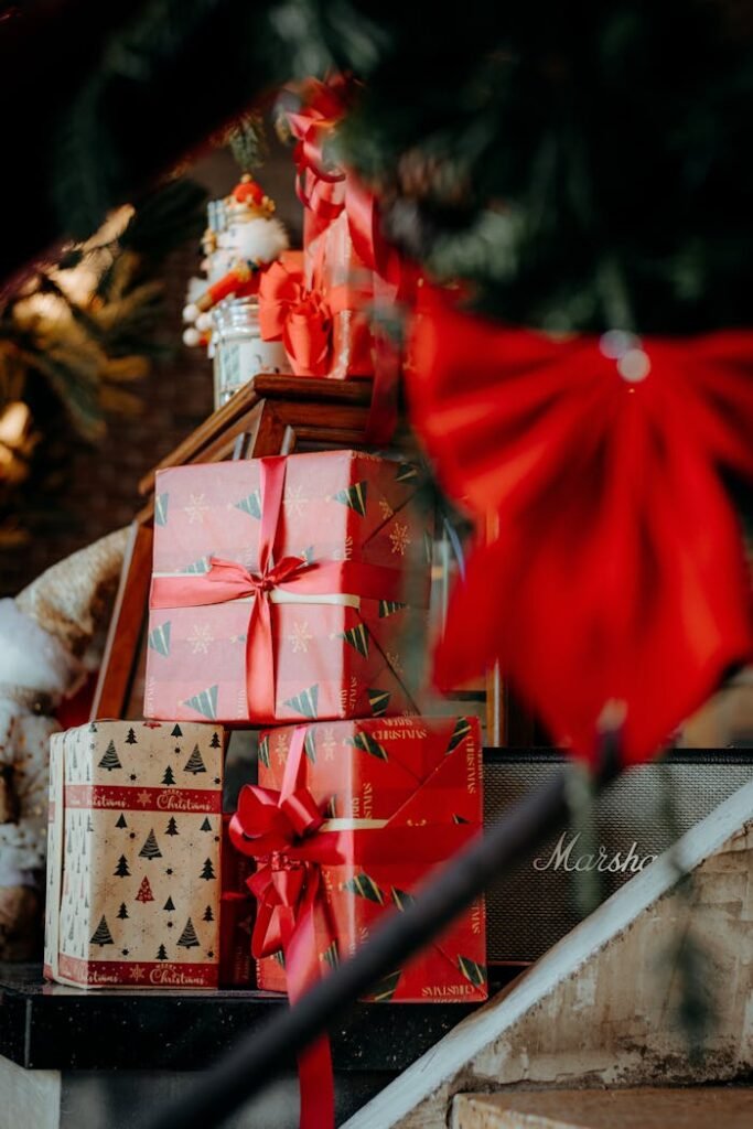 Stack of Christmas gifts with red ribbons under a decorated tree.