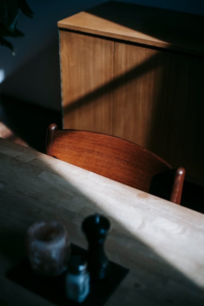From above of table with set of spices and chair placed near retro wooden vintage cabinet under sunlight in light room at  home