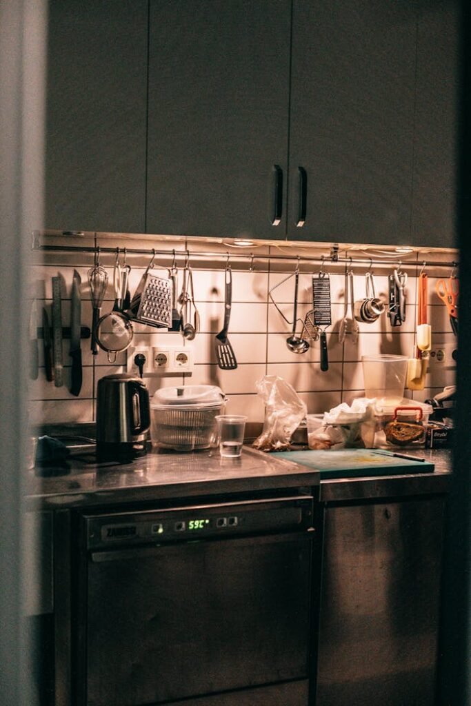 Kitchen interior with cupboards and various appliances hanging on hooks in dark kitchen with stove and dishware on table top